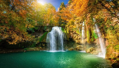 Stunning waterfall in the woods cascading into a glowing emerald lake embraced by lush trees