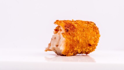 Close-up of a crispy fried croquette with a golden texture and creamy filling, set on a white...