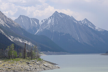 Mountain lake bordered by pine trees and steep rocky peaks under overcast skies in Banff National Park, Canada