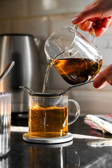 Pouring black tea in a glass mug
