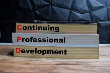 Books with words CPD - Continuing Professional Development on wooden table and black background