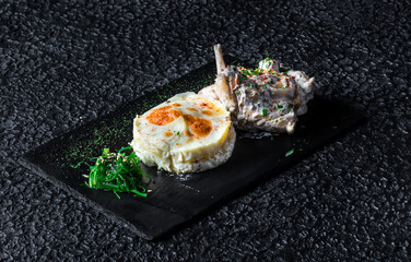 Delicious gourmet meat dish with potatoes and vegetables on a black plate.