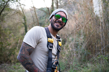 Smiling climber wearing safety harness and sunglasses in forest