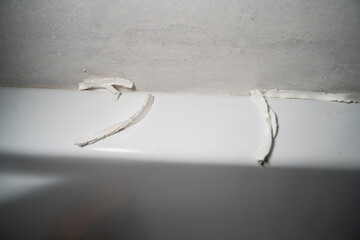 Poor quality white sealant in shower stall close-up. Removing sealant to replace and applying fresh...