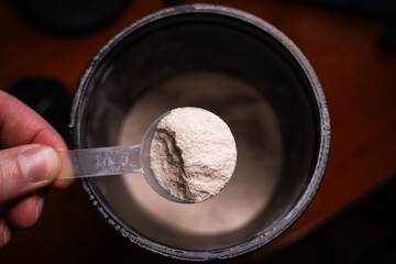 Hand holding a scoop with white powder on a background of a jar of powder. Sports nutrition intake