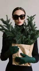 Fashionable model in sunglasses holds potted evergreen plants, showcasing modern style in a minimalistic indoor setting during winter