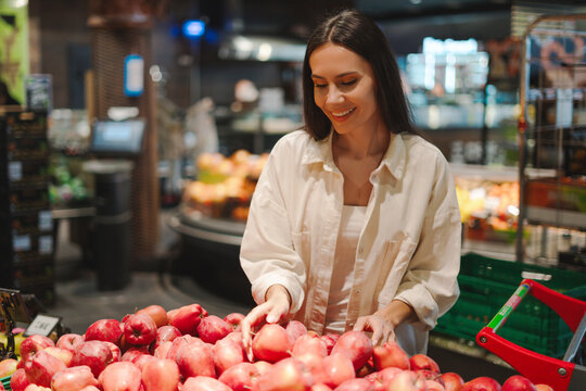 Beautiful, smiling Latin woman choosing red apples in supermarket