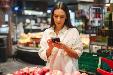 Woman using smartphone choosing apples in supermarket grocery store