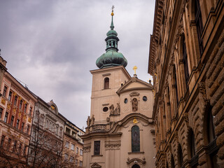 Church of St. Gall (Kostel sv. Havla) in Prague, baroque architecture surrounded by historic buildings on a cloudy day.