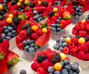 Colorful mix of fresh berries including strawberries, raspberries, blueberries, blackberries, and physalis in market trays, ideal for healthy eating and summer fruit concepts.