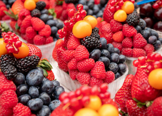Close-up of fresh berry mix with raspberries, strawberries, blackberries, redcurrants, blueberries, and golden physalis in a transparent container, ideal for healthy food and summer fruit themes.