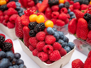 Close-up of fresh berry mix with raspberries, strawberries, blackberries, redcurrants, blueberries, and golden physalis in a transparent container, ideal for healthy food and summer fruit themes.