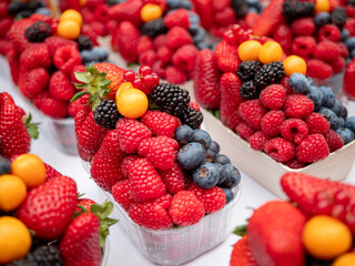 Obraz premium Colorful mix of fresh berries in a paper tray, including raspberries, blueberries, blackberries, strawberries, redcurrants and physalis, perfect for healthy eating and summer market themes.