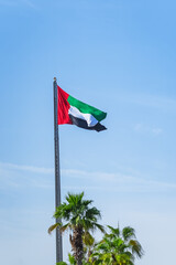 Dubai. A UAE flag waves in the breeze under a clear blue sky, proudly displaying national identity. vertical