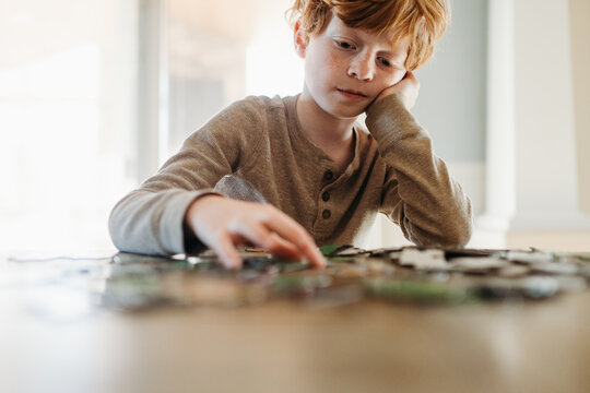 Boy sits at table putting together jigsaw puzzle at home