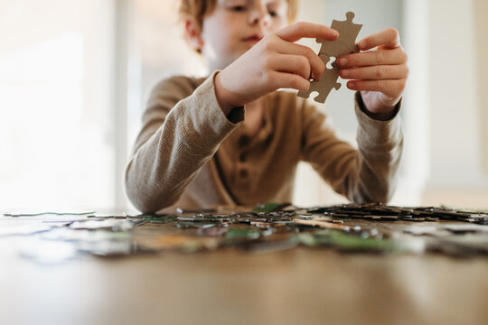 Boy putting pieces of puzzle together at home at kitchen table
