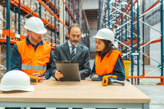 Manager showing inventory report to warehouse workers