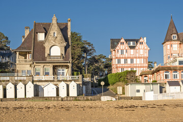 A beach at low tide with wet sand that reflects the buildings with traditional architecture  A row of beach huts typical of seaside resorts at Saint-Cast-Le-Guildo in Brittany, France
