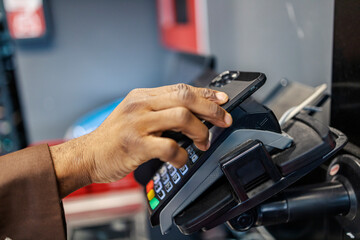 Close up of interracial man's hand with mobile phone using pos terminal for checkout at supermarket.