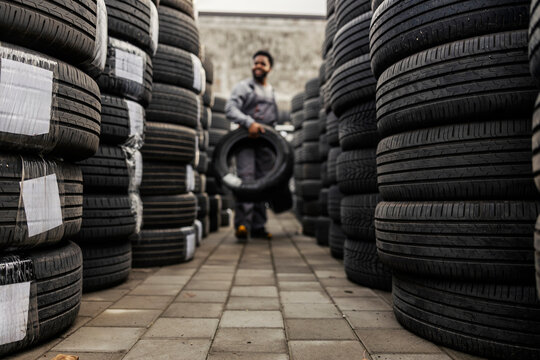 Selective focus on piles of tire with african american auto mechanic carrying tires in a blurry background.