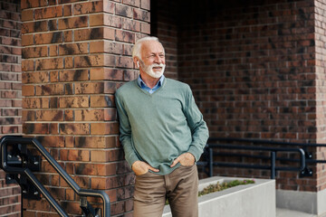 Portrait of casual trendy senior man leaning on the wall on city street and enjoying music.