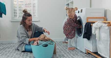 In a cozy bathroom, a mother and her daughter are loading clothes into a washing machine. The...