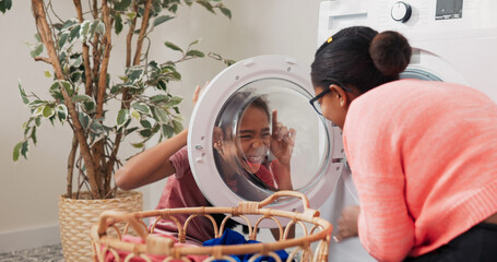 A joyful little girl crouches in front of the washing machine, smiling as her mother imitates her...