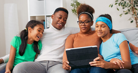 Parents and daughters enjoy quality time on the couch. They laugh and wave at the tablet camera while having a friendly conversation with people close to their hearts.