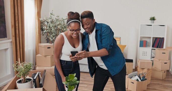 Delighted man runs up to his sweetheart who is cleaning up after moving shows phone, messages, photo on social media he is surprised smiling