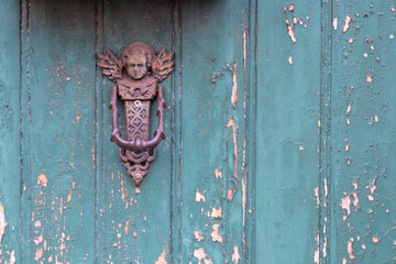 Vintage crackled- chipping paint wooden outside door, weathered and peeled by time background with a old metal knocker in a shape of a angel