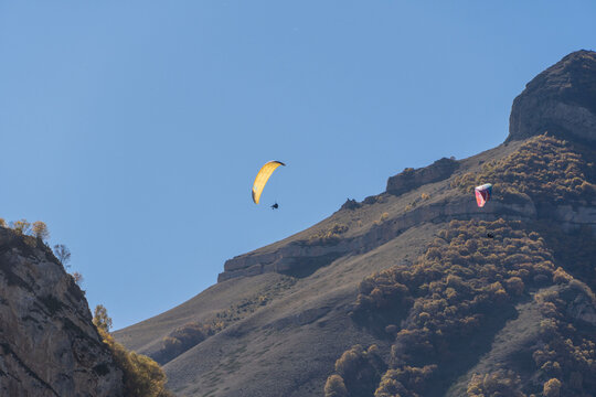 Paragliders enjoy of magnificent mountain landscapes from bird's eye view. Fly Chegem paragliding site in Chegem Gorge is new "Mecca" for extreme sports enthusiasts. El-Tyubu, Russia - October 7, 2024