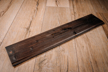 A single piece of burned wood panel with visible knots and charred texture lies on a light wood floor, showcasing a scorched, rustic finish..