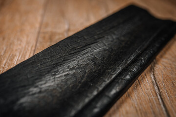 Close-up of a dark burnt wooden molding with visible grain texture and charred finish, placed on a...