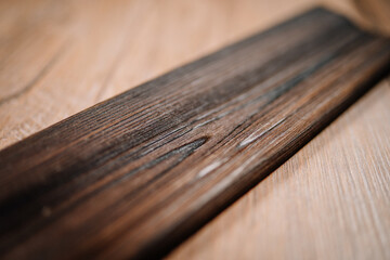 Close-up of a dark wooden molding plank with a weathered texture, placed diagonally on a light wood surface for contrast and detail..