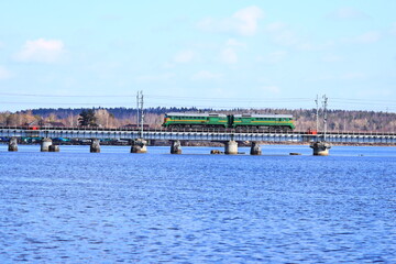 Obraz premium A train crosses a bridge over a river, with the water and surrounding landscape visible below.