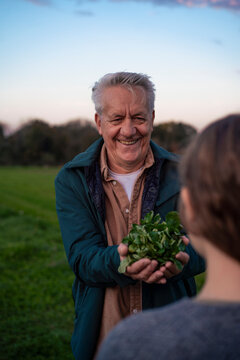 Grandfather smiling and holding greenery while interacting with granddaughter outdoors
