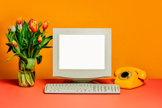 Vintage 80s workspace with CRT monitor, dial phone, and tulips in vase