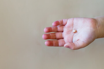 Little girl's hand holding and showing her fallen milk front tooth close up.