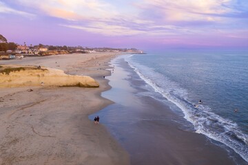 People enjoy the beach at sunset in Santa Cruz, California, USA. Surfers ride the waves while others walk along the shore, enjoying the peaceful coastal scenery.