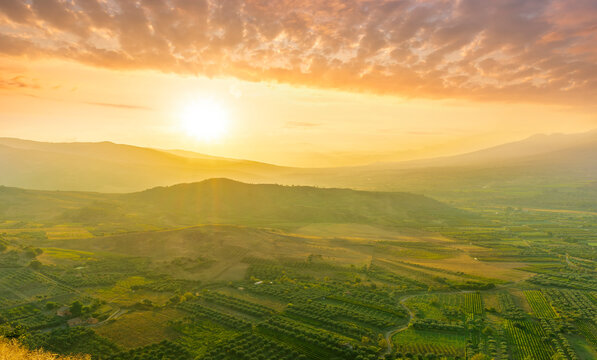 scenic rustic landscape with green hills and farms in a mountain valley during colorful cloudy sunset - Powered by Adobe