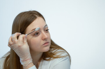 A young white woman is looking at a mirror, holding a brush for cleaning eyebrows with foam. Self-grooming beauty salon at home concept.