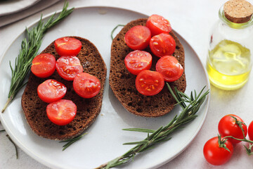 Black bread with cherry tomatoes in a plate on the table. Rosemary herb is nearby