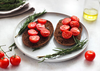 Black bread with cherry tomatoes in a plate on the table. Rosemary herb is nearby