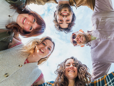 Friends Smiling in Circle Looking Down at Camera Outdoors - Happy group of friends standing in a circle, smiling and looking down at the camera on a sunny day - friendship and union concept