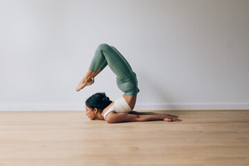 Young woman practicing yoga performing backbend on wooden floor