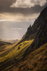 Autumn light bathes the Quiraing on Skye, casting long shadows over its dramatic cliffs and rolling hills. The landscape glows with golden hues, a breathtaking Highland scene.