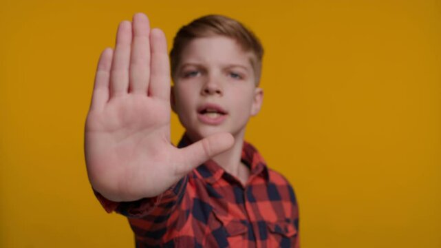 Boy Shows Palm at Camera Saying 'Wait' on Yellow Background