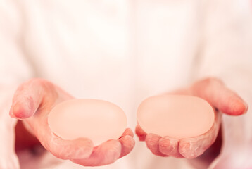 Close-up of a woman hands in transparent gloves holding silicone round breast implants. Breast...
