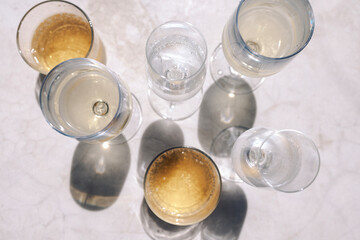 Glasses with various chilled alcoholic beverages on the marble table. Top view. Mineral water and champagne. Fragrant sparkling wines in bright sunlight. Copy space