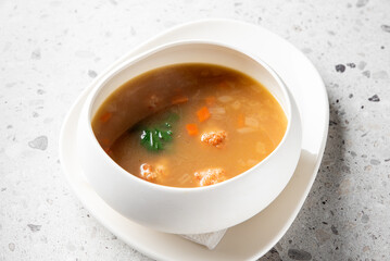 A steaming bowl of savory soup featuring vibrant vegetables and tender meatballs. Served in an...